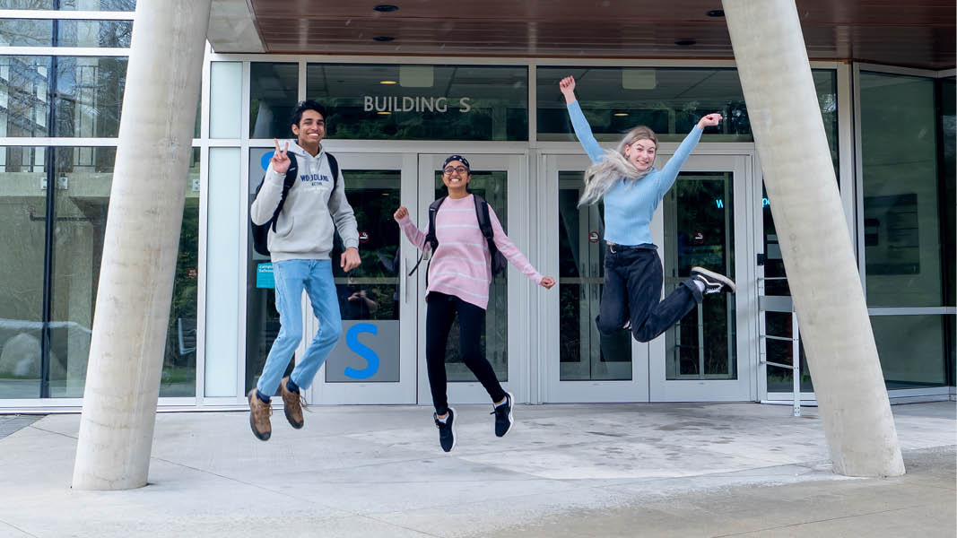 Three UFV students jump high in front of the SUS building.