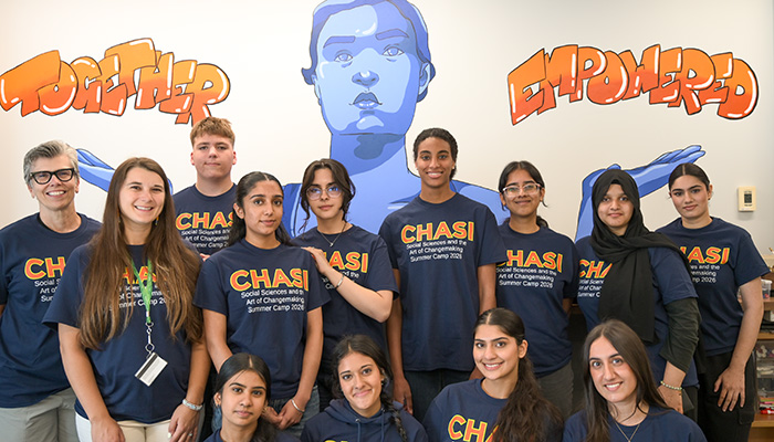 Photo of 10 students and three members of the CHASI team all wearing CHASI Summer Camp t-shirts, and posing in front of CHASI's Together Empowered mural