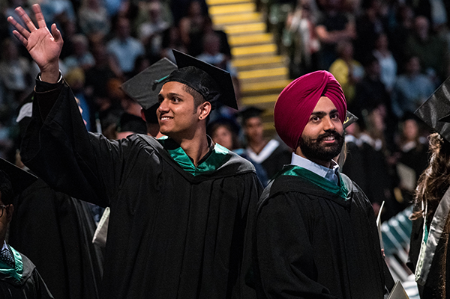 Two young graduates, smiling and waving at Convocation.