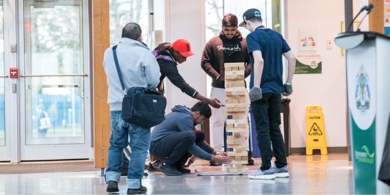 A group of students play a game of Jenga with giant wooden blocks