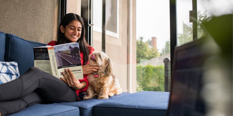 UFV student reading on her couch, cuddling a puppy.