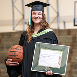 Smiling UFV grad holds an award and her basketball.