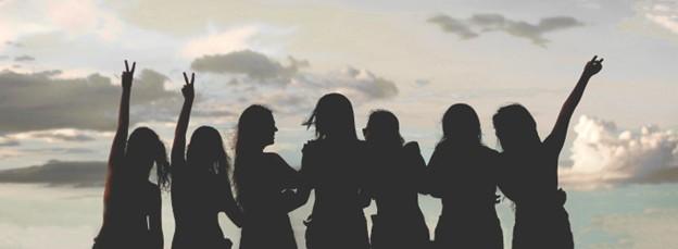 silhouette of women arm and arm in front of clouds