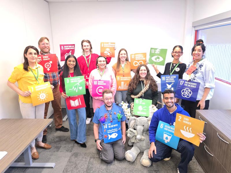 11 team members of the office of sustainability smile at the camera holding up the symbols for the united nations sustainable development goals