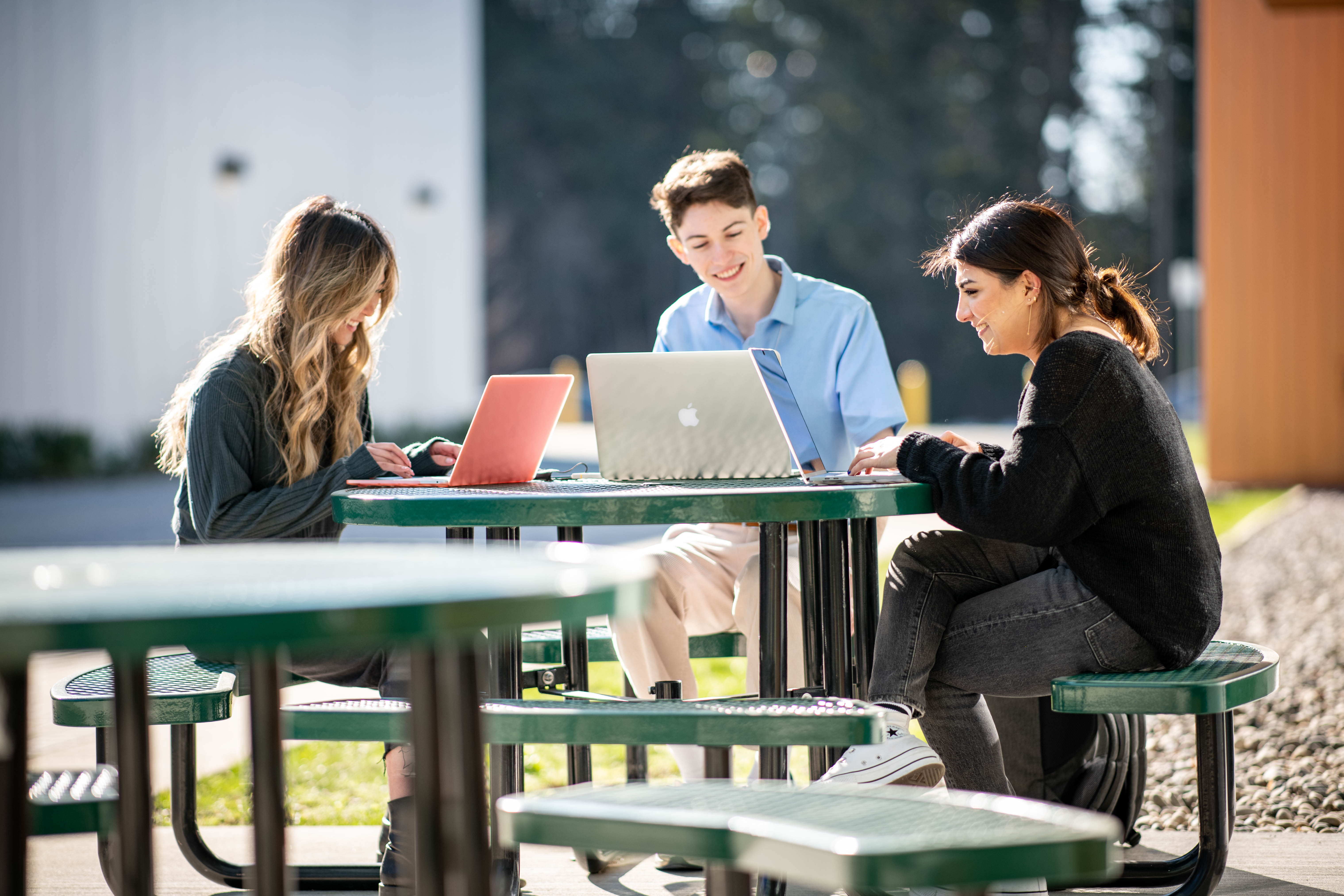 3 students on their computers on campus in front of building S