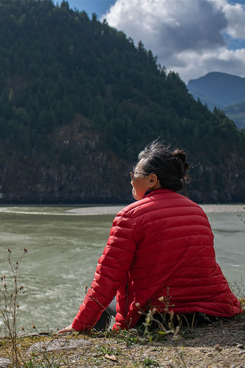 A woman sits on the banks of the Vedder river with a mountain in the background.