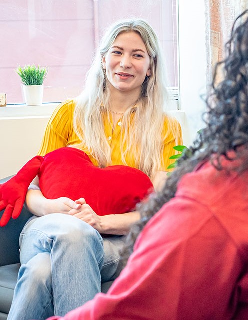 A student sits in a comfy chair chatting and hugging a heart-shaped pillow