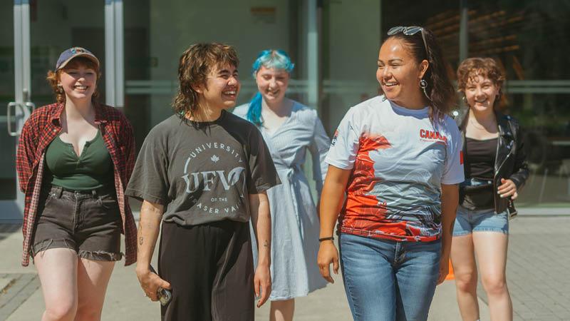 Four students walking together on the UFV campus. They are a diverse group, smiling and talking.