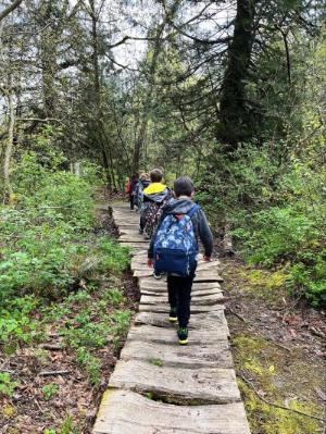 Children walk along a wooden walkway through the forest