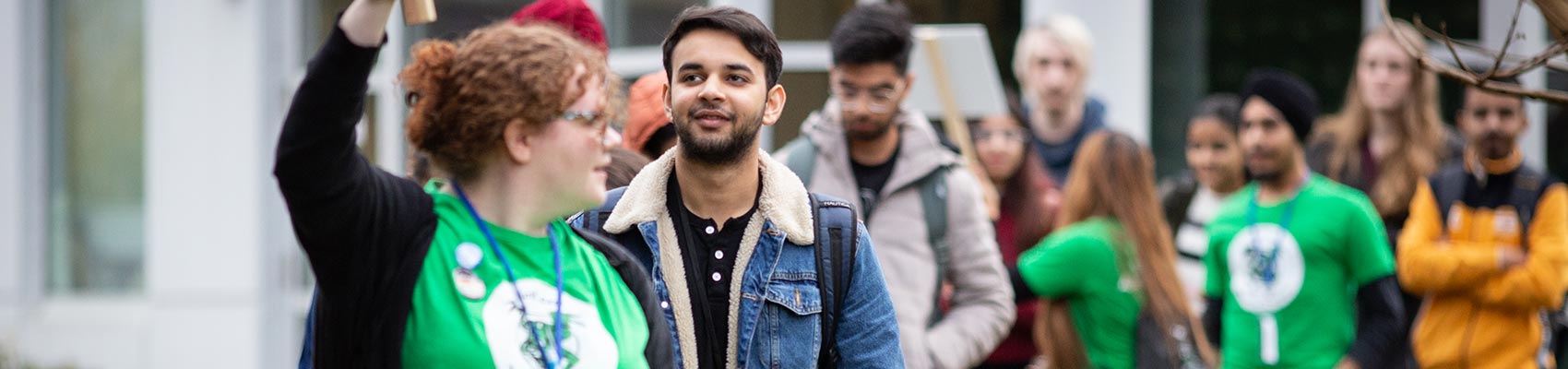 A young women in a green shirt is leading a group of students on a campus orientation tour.